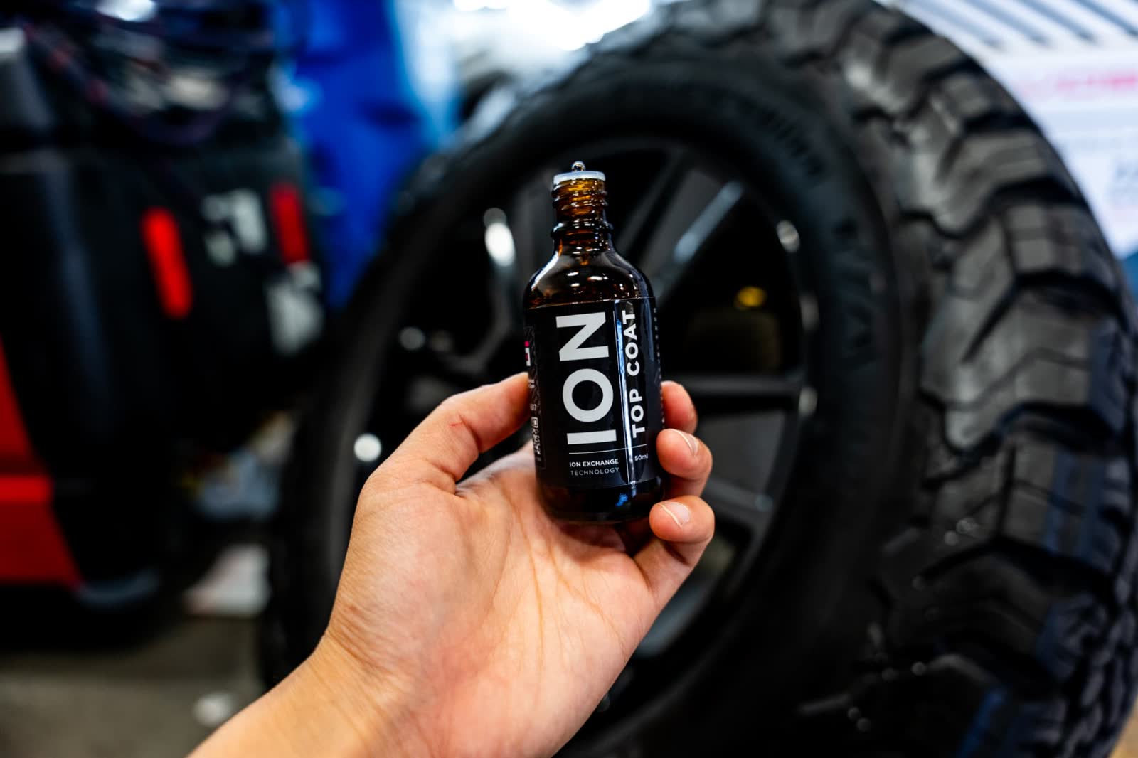 Bottle of ION Top Coat ceramic coating held in front of a truck wheel at Lusso Auto Design
