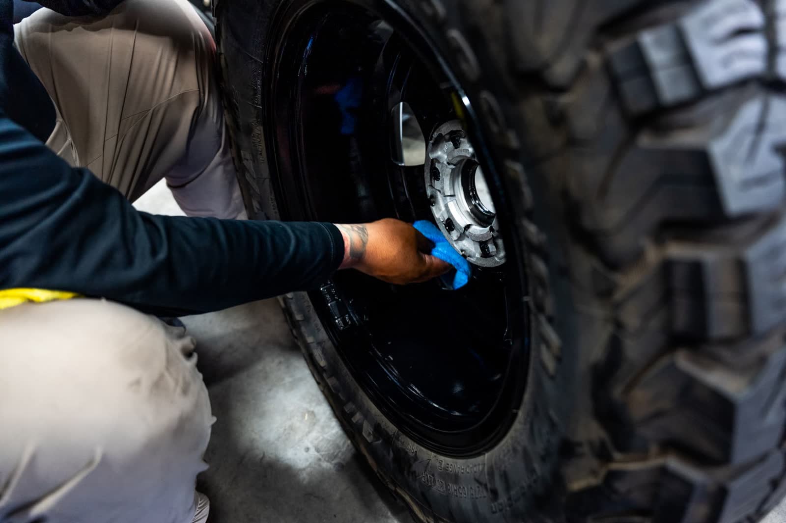 Technician leveling ceramic coating on a gloss black off road wheel with a microfiber towel