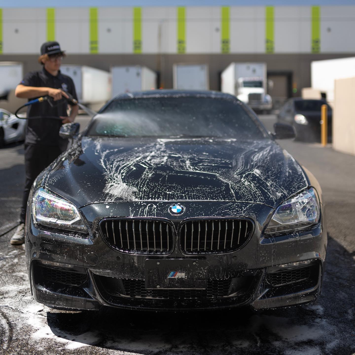Lusso technician foam washing a black BMW 6 Series outside the Henderson shop