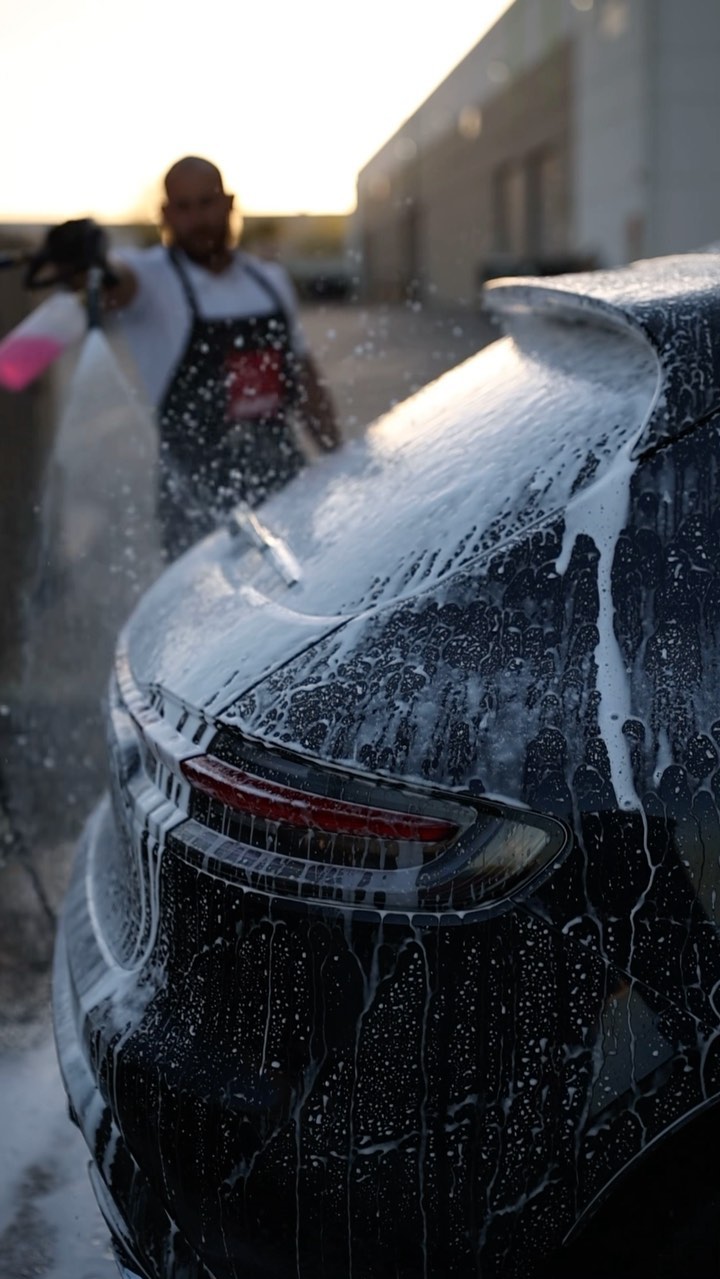 Porsche rear end covered in snow foam during a maintenance wash at sunset