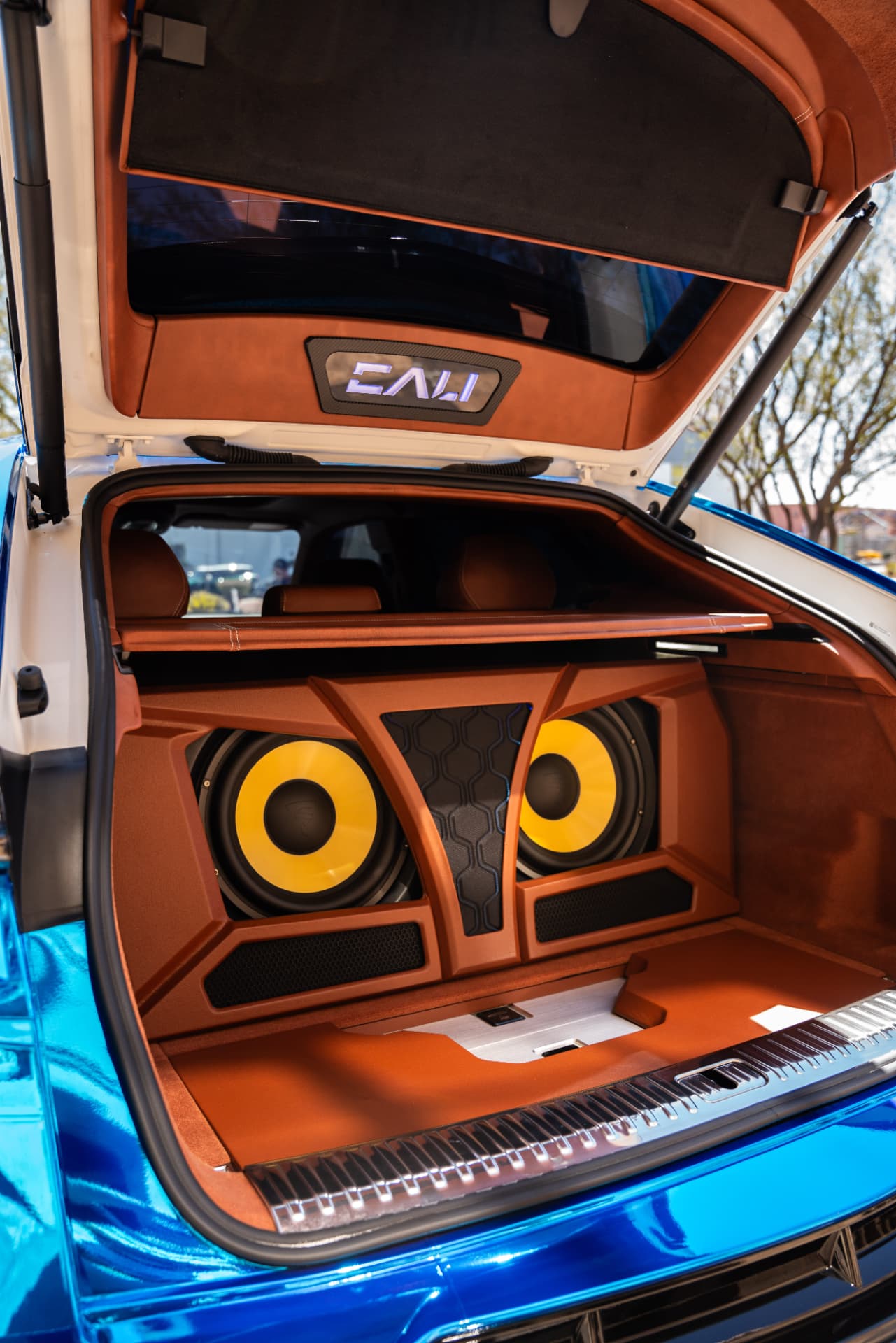 Cognac suede trunk build with dual yellow cone subwoofers and lit CALI badge in a blue chrome SUV
