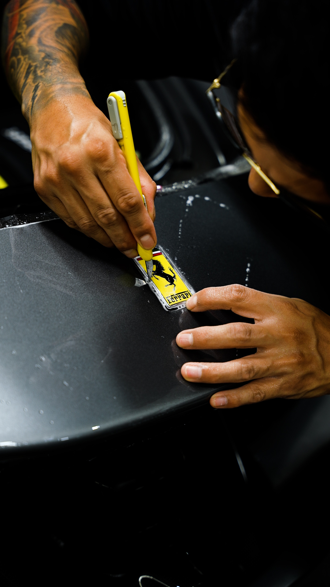 Lusso technician hand-trimming paint protection film around the badge on a satin grey Ferrari SF90 in Henderson